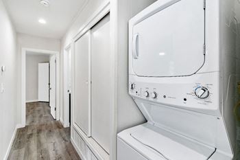 A white washing machine is in a hallway with wood floors in an apartment at Wescove Apartments